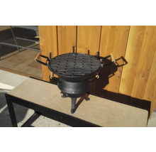 Grătar pe cărbuni din fontă cu trei picioare și mânere din lemn în fața unui perete din lemn.