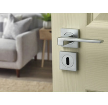 Set de mâner pentru ușă modern cu rozete pătrate cu aspect de oțel inoxidabil, montat pe o ușă din lemn deschisă.