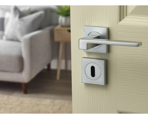 Set de mâner pentru ușă modern cu rozete pătrate cu aspect de oțel inoxidabil, montat pe o ușă din lemn deschisă.