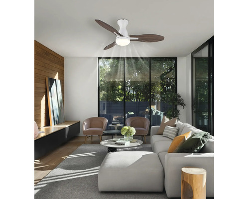 Ventilator de tavan modern cu iluminat și trei palete din lemn într-o sufragerie luminoasă cu canapea și ferestre mari.