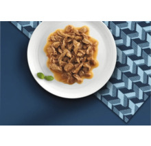 Hrană umedă pentru pisici cu bucățele de carne în sos servită pe o farfurie.