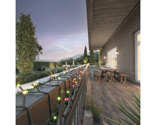 Ghirlandă luminoasă LED colorată pentru exterior, înfășurată pe o balustradă de balcon pe o terasă de lemn cu masă și bănci la amurg.