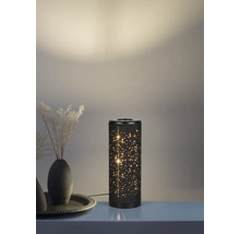 Veioză cilindrică din metal negru cu model de stele perforate și efect de lumină caldă într-un decor.