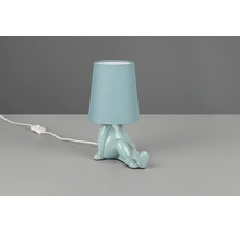 Veioză cu bază din ceramică albastru deschis în formă de figură care șade și abajur din material textil albastru deschis.
