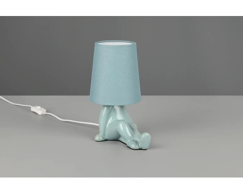 Veioză cu bază din ceramică albastru deschis în formă de figură care șade și abajur din material textil albastru deschis.