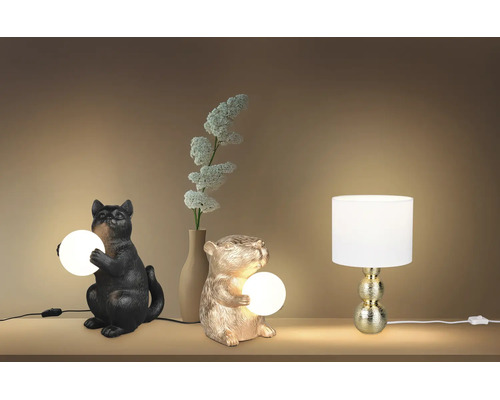 Trei lămpi de masă decorative: o pisică neagră și un hamster auriu cu sfere luminoase și o lampă cu abajur alb și picior auriu.