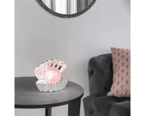 Veioză decorativă în formă de scoică argintie cu o perlă roz luminoasă pe o masă rotundă într-o sufragerie.