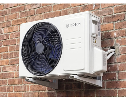 Unitate exterioară Bosch pentru aer condiționat sau pompă de căldură cu Bosch Logo, montată pe un perete de cărămidă cu suporturi și racorduri.