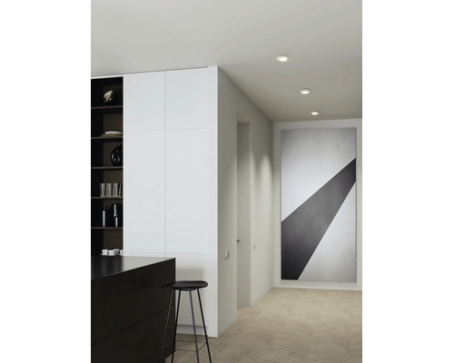 Spațiu de locuit modern cu spoturi încastrate pe hol, bucătărie minimalistă, scaun de bar și tablou abstract pe parchet tip brăduț.