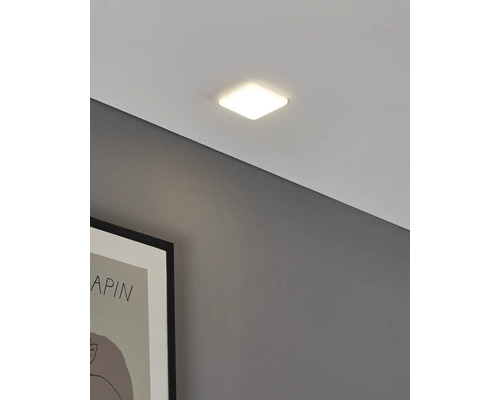 Plafonieră LED pătrată modernă cu design plat, aprinsă și montată pe tavan lângă un tablou înrămat.