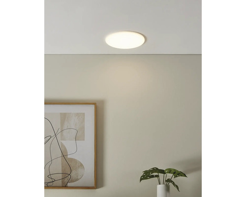 Plafonieră LED rotundă și plată într-o cameră mobilată modern cu un tablou pe perete și o plantă de apartament.