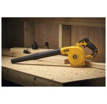 Suflantă cu acumulator DeWalt pe un banc de lucru din lemn într-un atelier cu așchii de lemn și diferite duze.