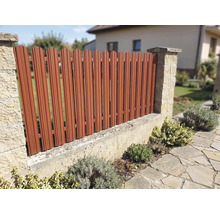 Gard metalic pentru grădină cu lamele verticale între stâlpi de piatră, montat pe un zid mic într-o grădină.