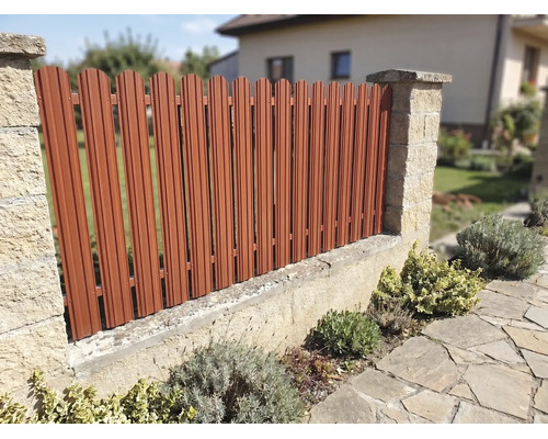 Gard metalic pentru grădină cu lamele verticale între stâlpi de piatră, montat pe un zid mic într-o grădină.