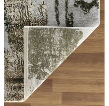 Covor modern cu fir scurt, cu model abstract pe podea de lemn, colț pliat cu spatele vizibil.