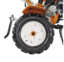 Vedere de aproape a unei roți de motocultor cu profil adânc și jantă albă, inclusiv părți ale motorului și carcasei portocalii.