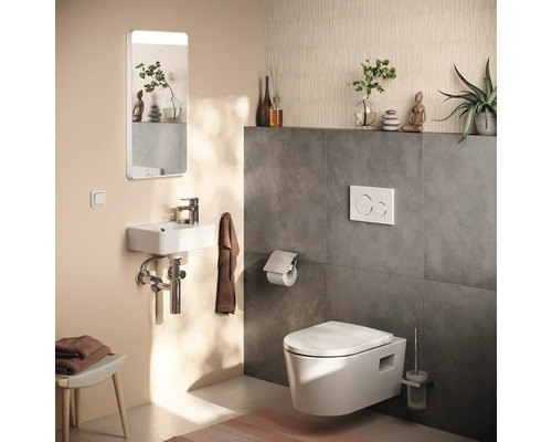 Toaletă modernă pentru oaspeți cu WC suspendat, lavoar mic, oglindă cu iluminare și faianță cu aspect de beton.