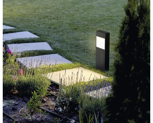 Lampă de exterior neagră modernă pentru iluminarea aleilor într-o grădină cu dale și levănțică.