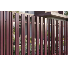 Gard metalic vertical modern cu șipci profilate de culoare roșu închis în fața unei case moderne și a vegetației din grădină.