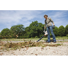 Femeie care folosește un suflător electric de frunze STIHL în grădină pentru a îndepărta frunzele de pe o alee de pietriș.