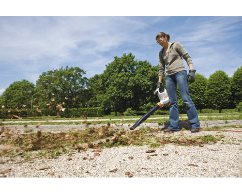 Femeie care folosește un suflător electric de frunze STIHL în grădină pentru a îndepărta frunzele de pe o alee de pietriș.