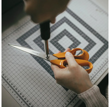 Reglarea unei foarfeci Fiskars cu o șurubelniță pe un covoraș de tăiere.