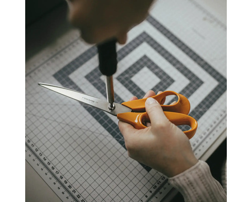 Reglarea unei foarfeci Fiskars cu o șurubelniță pe un covoraș de tăiere.
