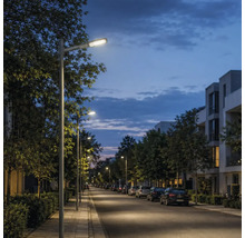 Stâlpi de iluminat moderni care luminează un trotuar și o stradă într-o zonă rezidențială la amurg.