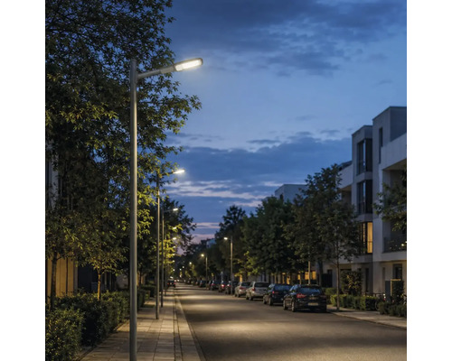 Stâlpi de iluminat moderni care luminează un trotuar și o stradă într-o zonă rezidențială la amurg.