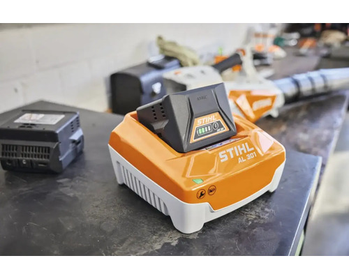 Încărcător rapid STIHL AL 301 cu acumulator AK 30 introdus pe un banc de lucru într-un atelier.