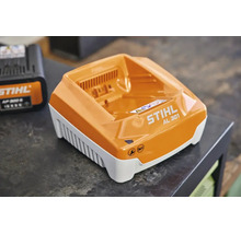 Încărcător rapid STIHL AL 301 cu indicator de întreținere și stare de încărcare pe un blat de lucru.