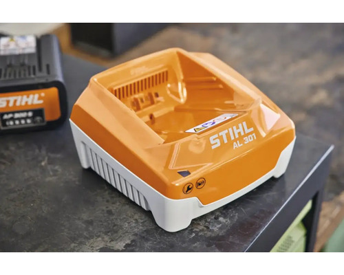 Încărcător rapid STIHL AL 301 cu indicator de întreținere și stare de încărcare pe un blat de lucru.