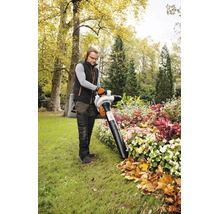 Un bărbat lucrează cu un aspirator de frunze STIHL într-o grădină luminoasă. El aspiră frunzele de toamnă dintr-un strat de flori plantat.