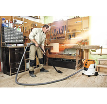 Un bărbat aspiră așchii de lemn cu un aspirator umed și uscat Stihl într-un atelier de tâmplărie luminos și organizat.