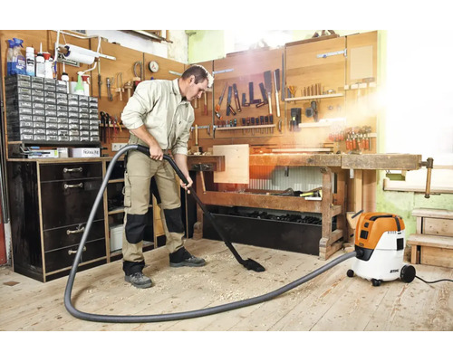 Un bărbat aspiră așchii de lemn cu un aspirator umed și uscat Stihl într-un atelier de tâmplărie luminos și organizat.