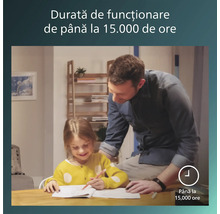 Un bărbat și o fetiță învață la o masă în lumină puternică. Textul indică o durată de funcționare de până la 15000 de ore.