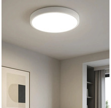 Plafonieră LED rotundă modernă, de culoare albă, montată într-o cameră luminoasă cu o ramă de tablou și un raft.