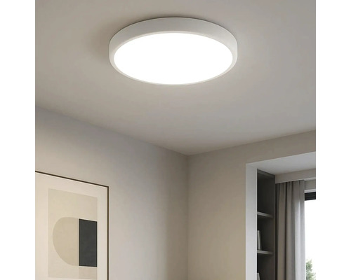 Plafonieră LED rotundă modernă, de culoare albă, montată într-o cameră luminoasă cu o ramă de tablou și un raft.