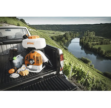 Atomizor Stihl cu Stihl Logo pe o camionetă cu echipament de protecție în fața unei podgorii luminoase și a unui râu în fundal.