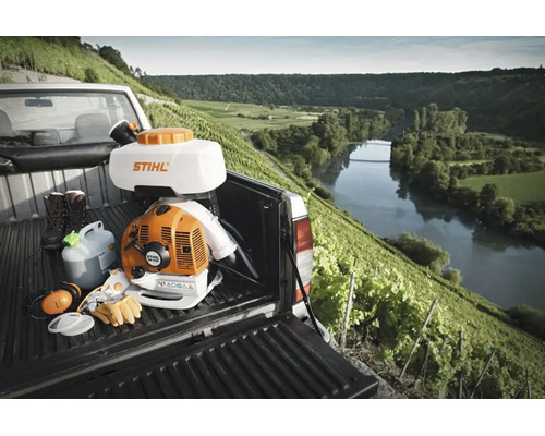 Atomizor Stihl cu Stihl Logo pe o camionetă cu echipament de protecție în fața unei podgorii luminoase și a unui râu în fundal.