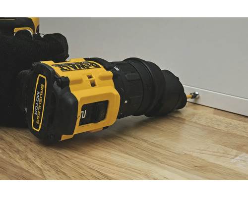 Mașină de găurit și înșurubat cu acumulator DeWalt cu atașament excentric înșurubează un șurub într-un panou alb pe o suprafață de lemn.
