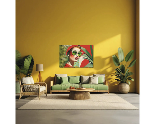 Sufragerie modernă cu perete galben, canapea verde, fotoliu din ratan și un tablou pop art cu o femeie cu ochelari de soare.