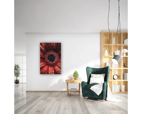 Sufragerie modernă și luminoasă cu tablou cu o gerbera cu picături de apă, fotoliu verde și bibliotecă din lemn.