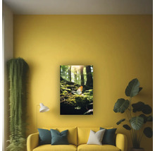 Tablou de perete cu motiv forestier și un fluture, așezat deasupra unei canapele într-o sufragerie luminoasă și organizată, cu plante de interior și o lampă.