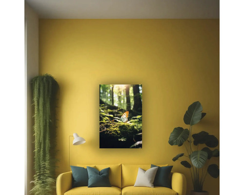 Tablou de perete cu motiv forestier și un fluture, așezat deasupra unei canapele într-o sufragerie luminoasă și organizată, cu plante de interior și o lampă.