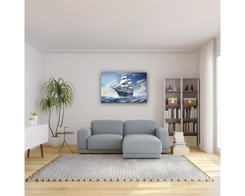 Living luminos cu tablou cu corabie deasupra unei canapele gri, podea din lemn, covor, raft pentru cărți și plantă de interior.