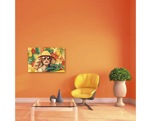 Cameră modernă cu tablou cu o femeie cu pălărie și ochelari de soare cu motiv tropical, fotoliu galben, masă de sticlă și plantă.