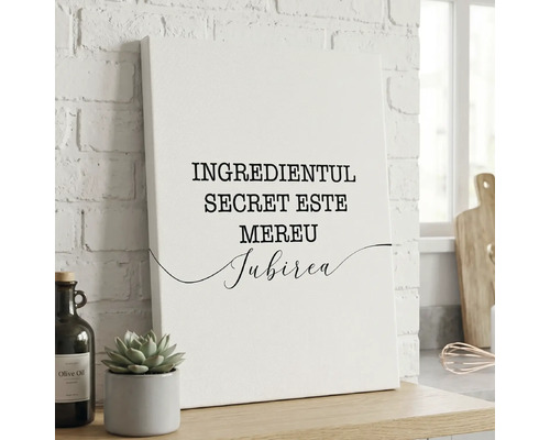 Tablou canvas cu textul Ingredientul secret este mereu iubirea așezat într-un decor de bucătărie lângă o plantă și o sticlă de ulei de măsline.