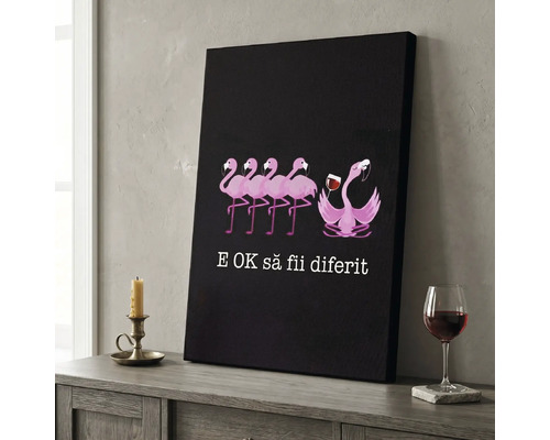 Tablou pe pânză cu flamingo roz, dintre care unul ține un pahar cu vin, și textul românesc E okay să fii diferit, pe o comodă.