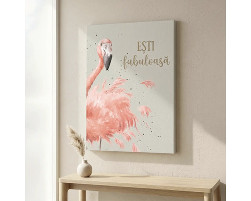 Tablou pe pânză cu ilustrația unui flamingo roz și textul ESTI fabuloasa deasupra unei mese de lemn într-o cameră luminoasă.